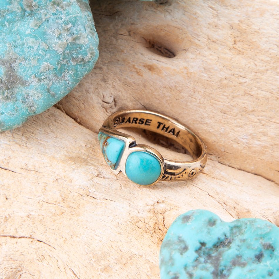 Gold ring with turquoise stones on a wooden surface with turquoise stones around