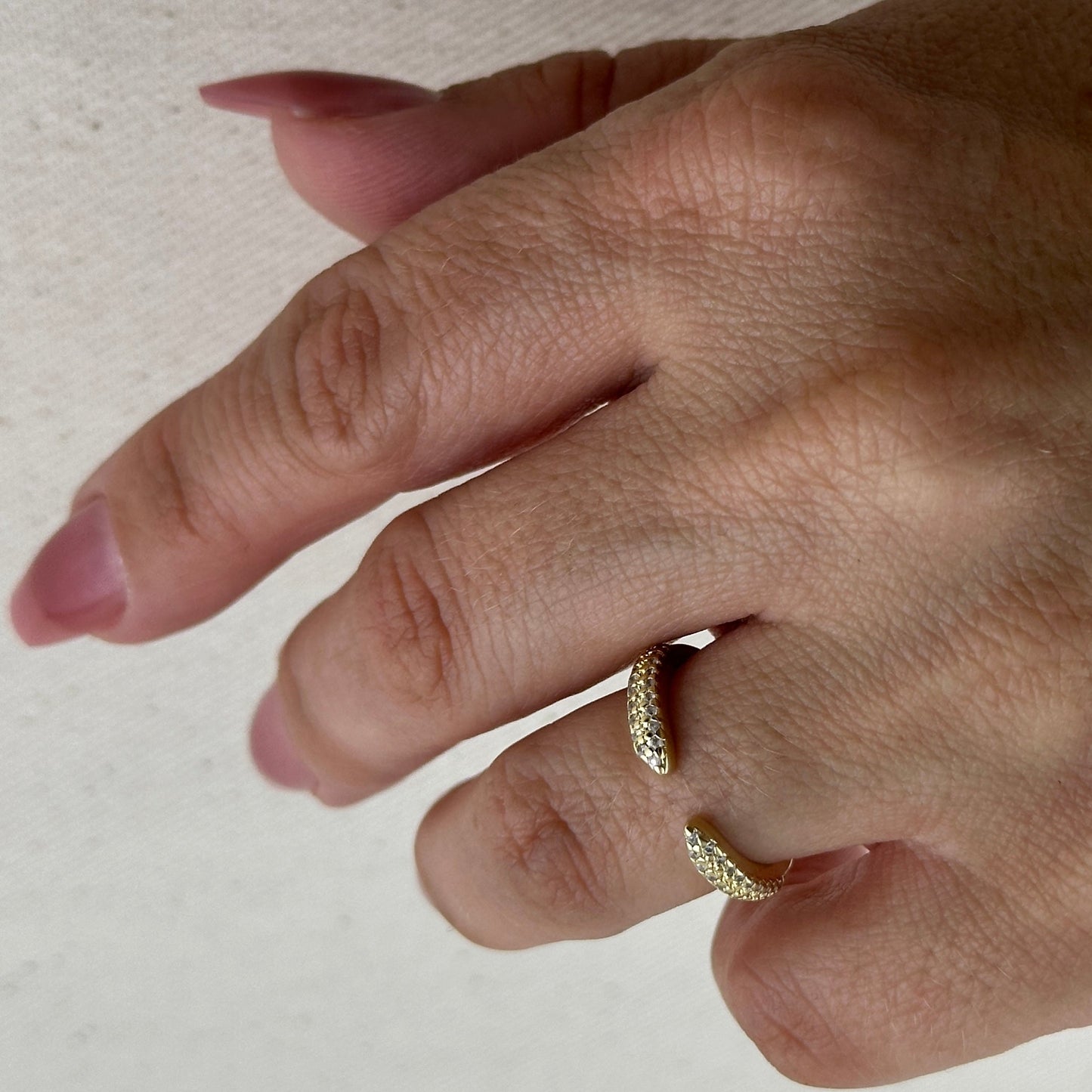 Close-up of a hand wearing two gold rings on a light background