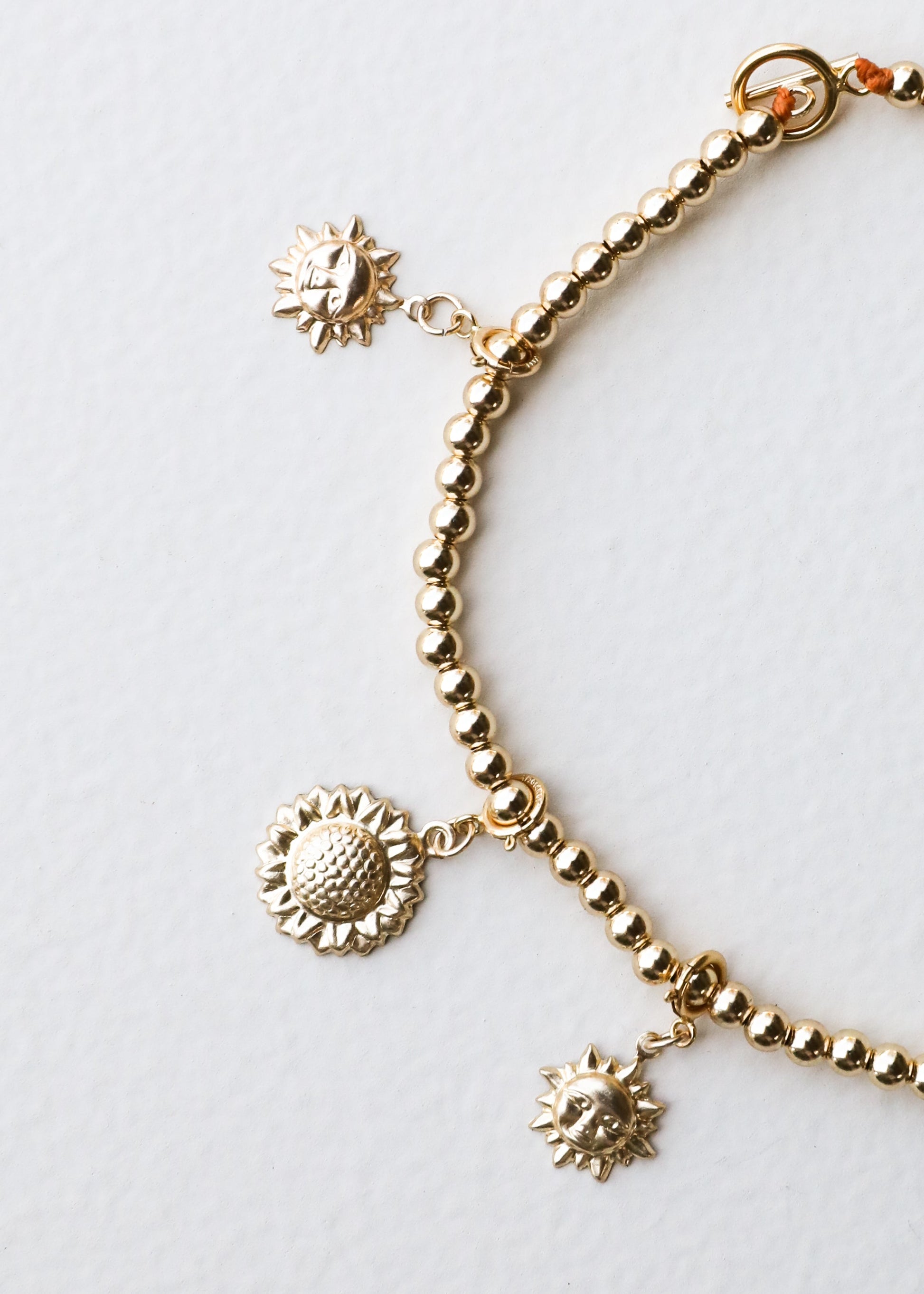 Gold bracelet with sunflower charms on a light gray background