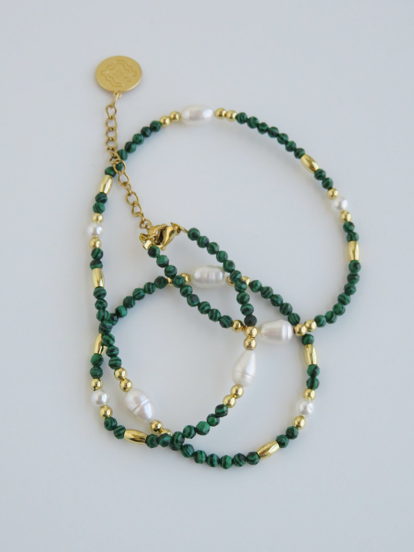 Green beaded necklace with gold accents on a light gray background