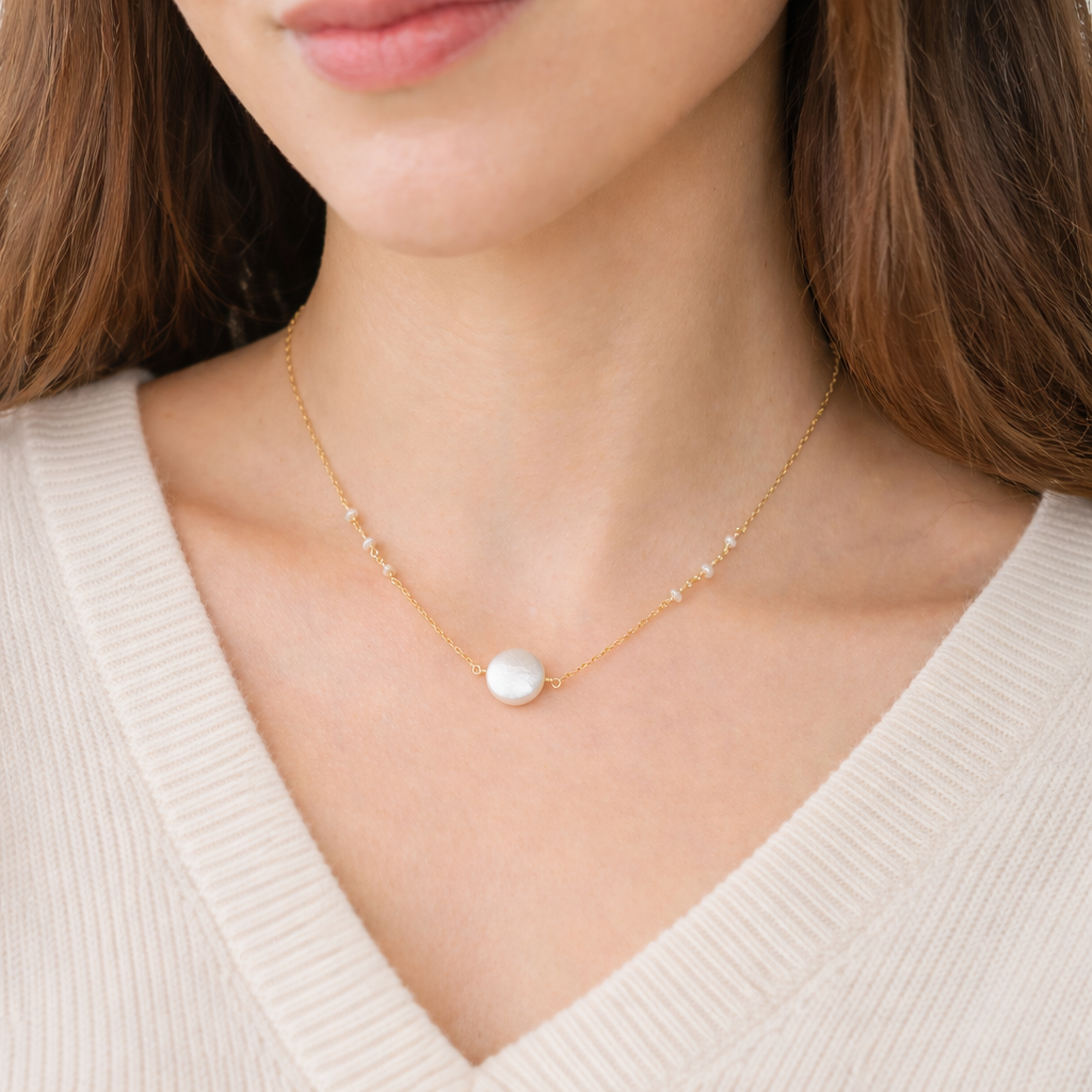 Gold necklace with a pearl pendant worn by a person in a beige sweater.