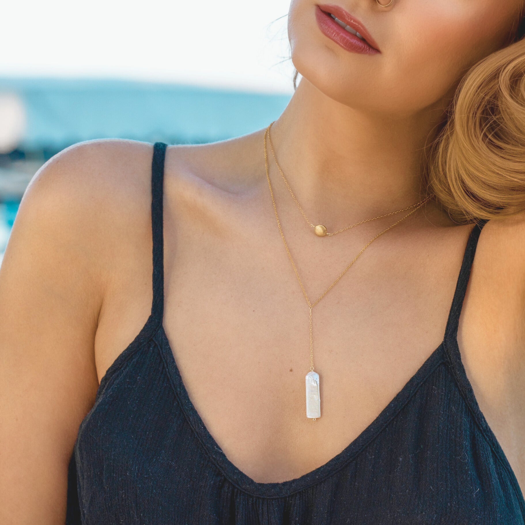 Woman wearing a necklace with a pendant against a blurred beach background
