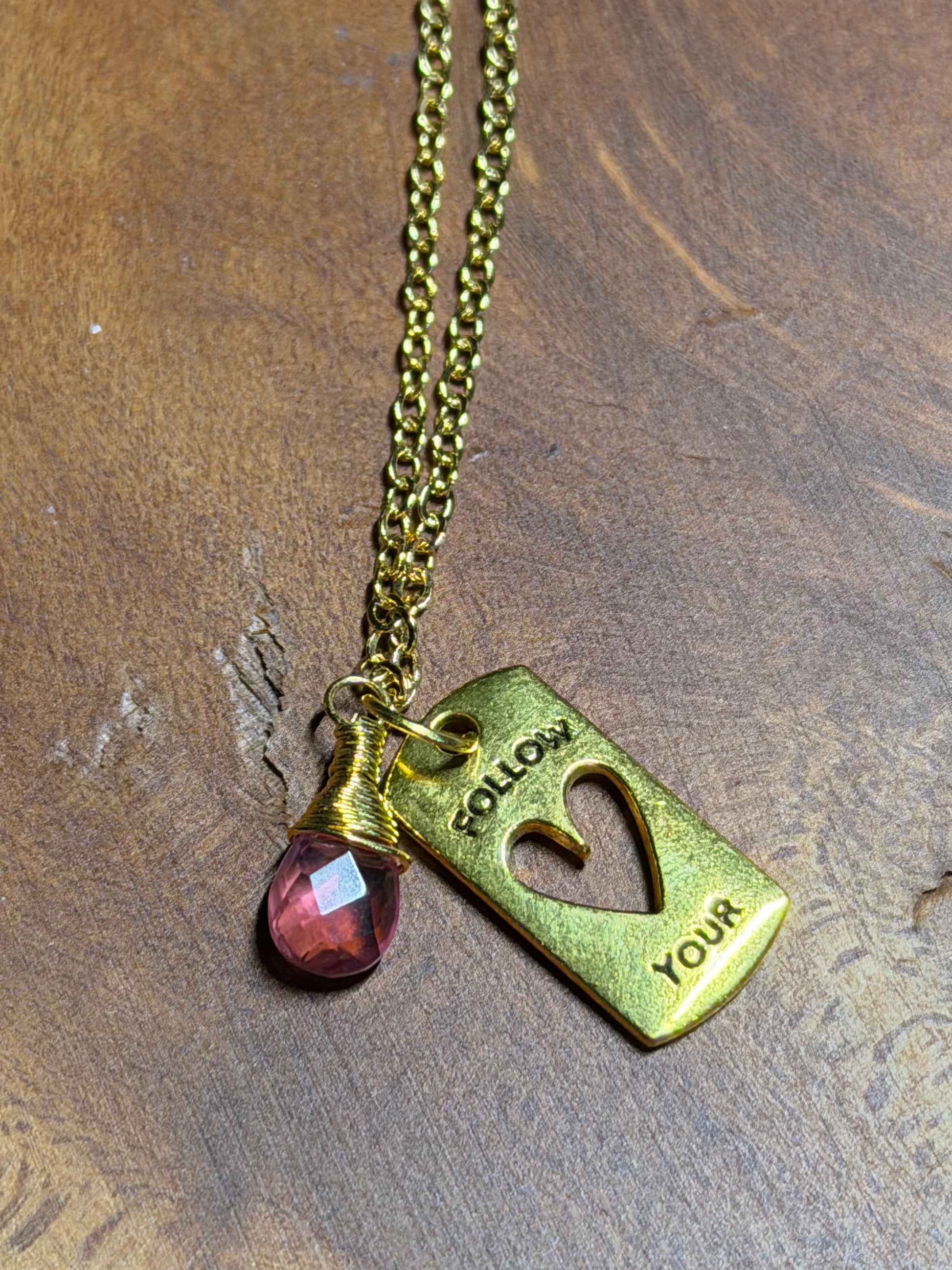 Gold necklace with a heart-shaped pendant and rose amethyst  gemstone on a wooden surface