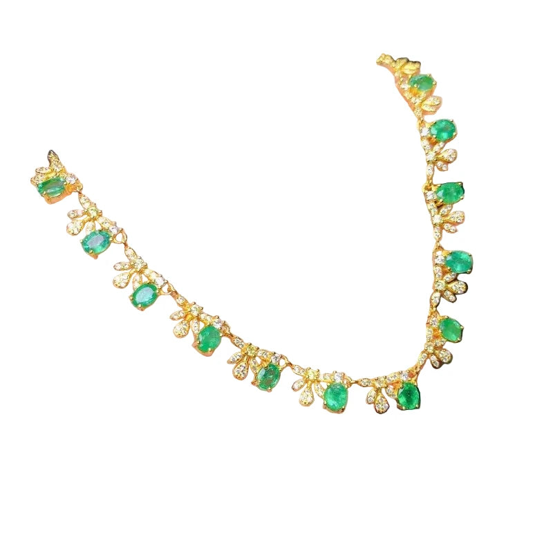 Gold necklace with green emerald gemstones on a hand against a dark background