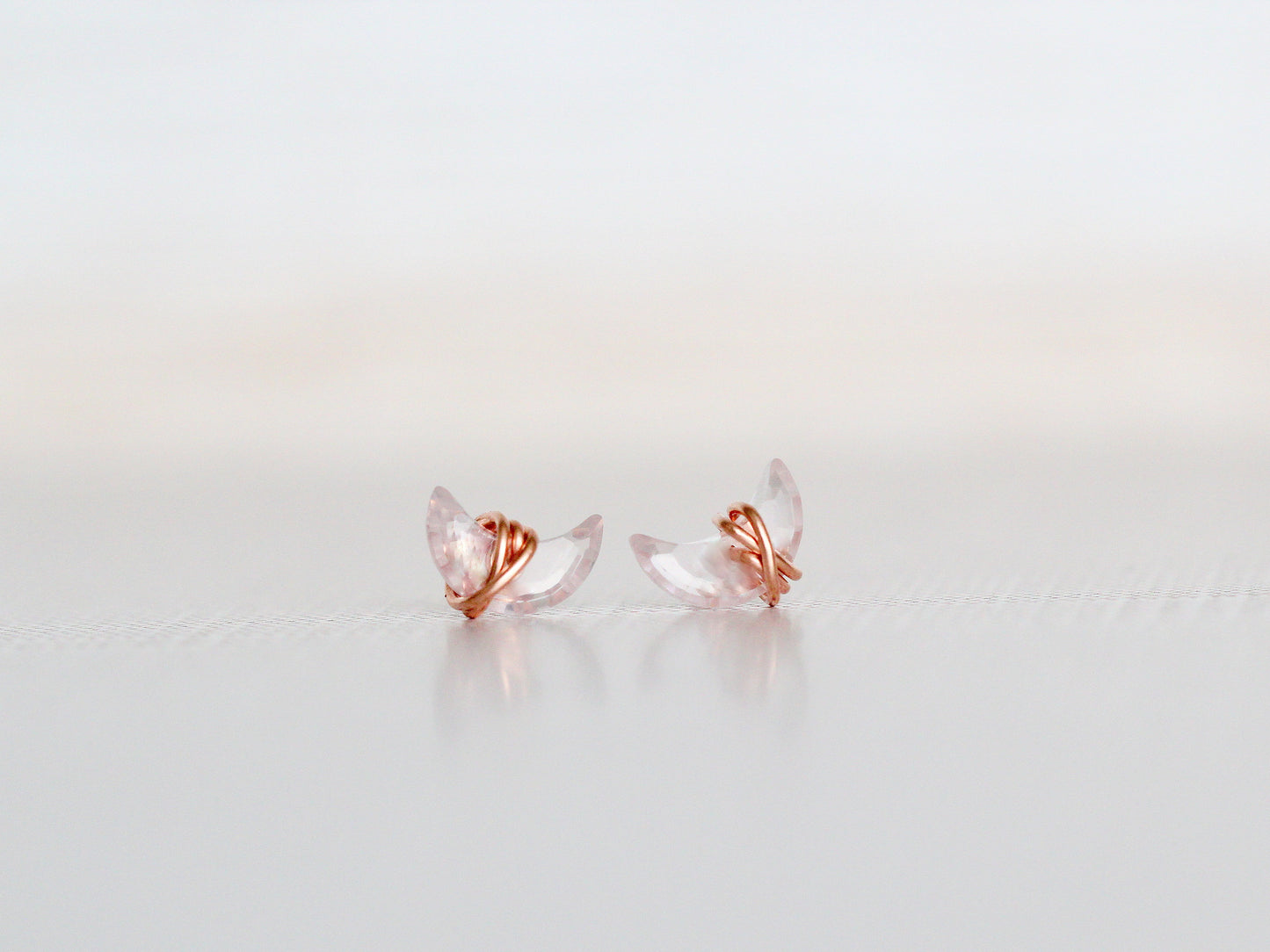 Pair of rose gold and clear crystal earrings on a light gray background