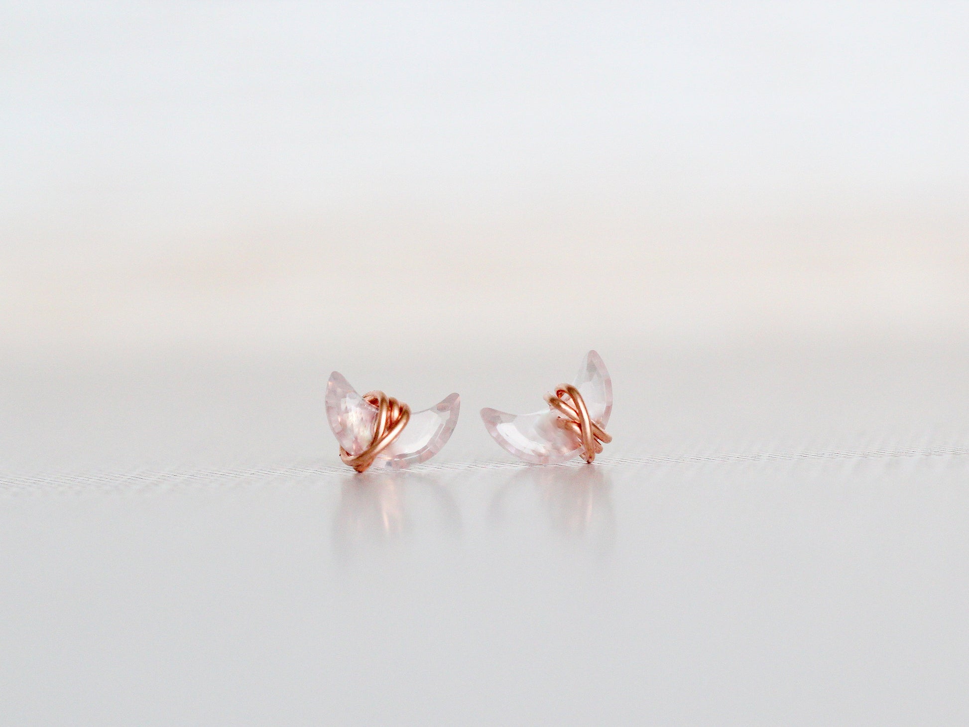 Pair of rose gold and clear crystal earrings on a light gray background