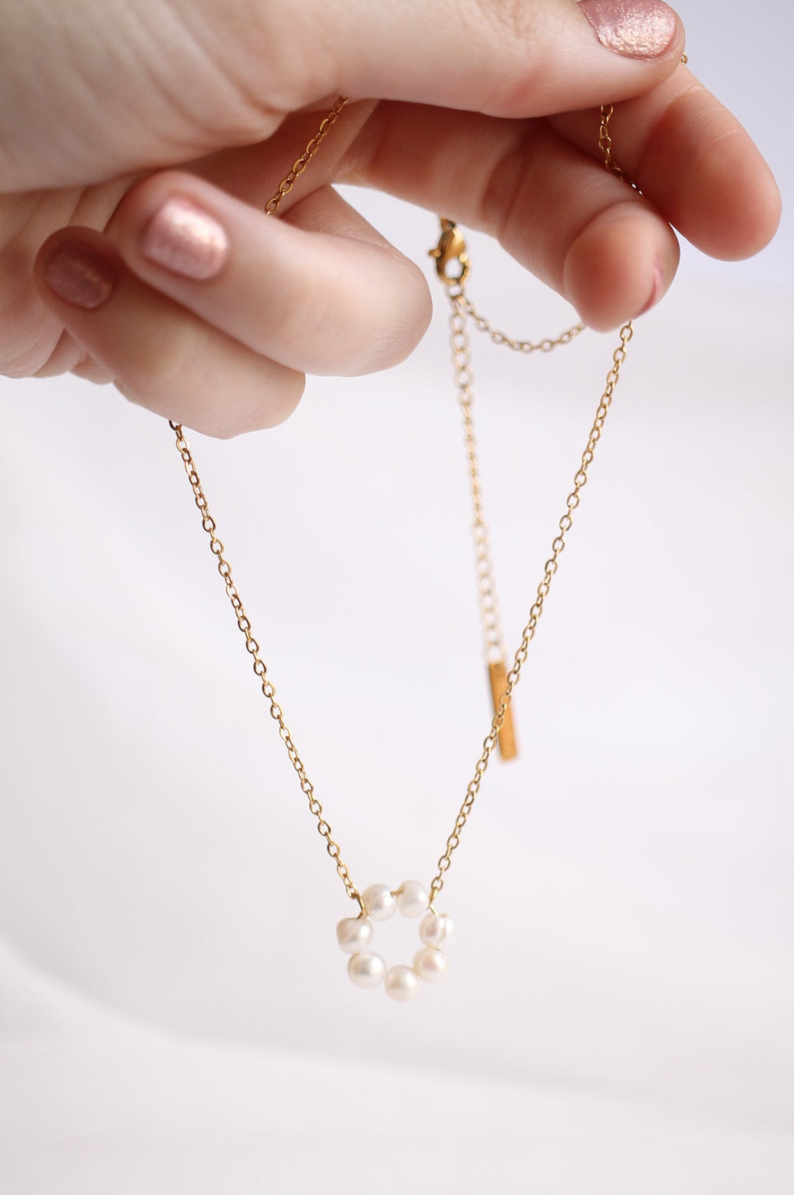 Hand holding a delicate necklace with a small pendant on a light background