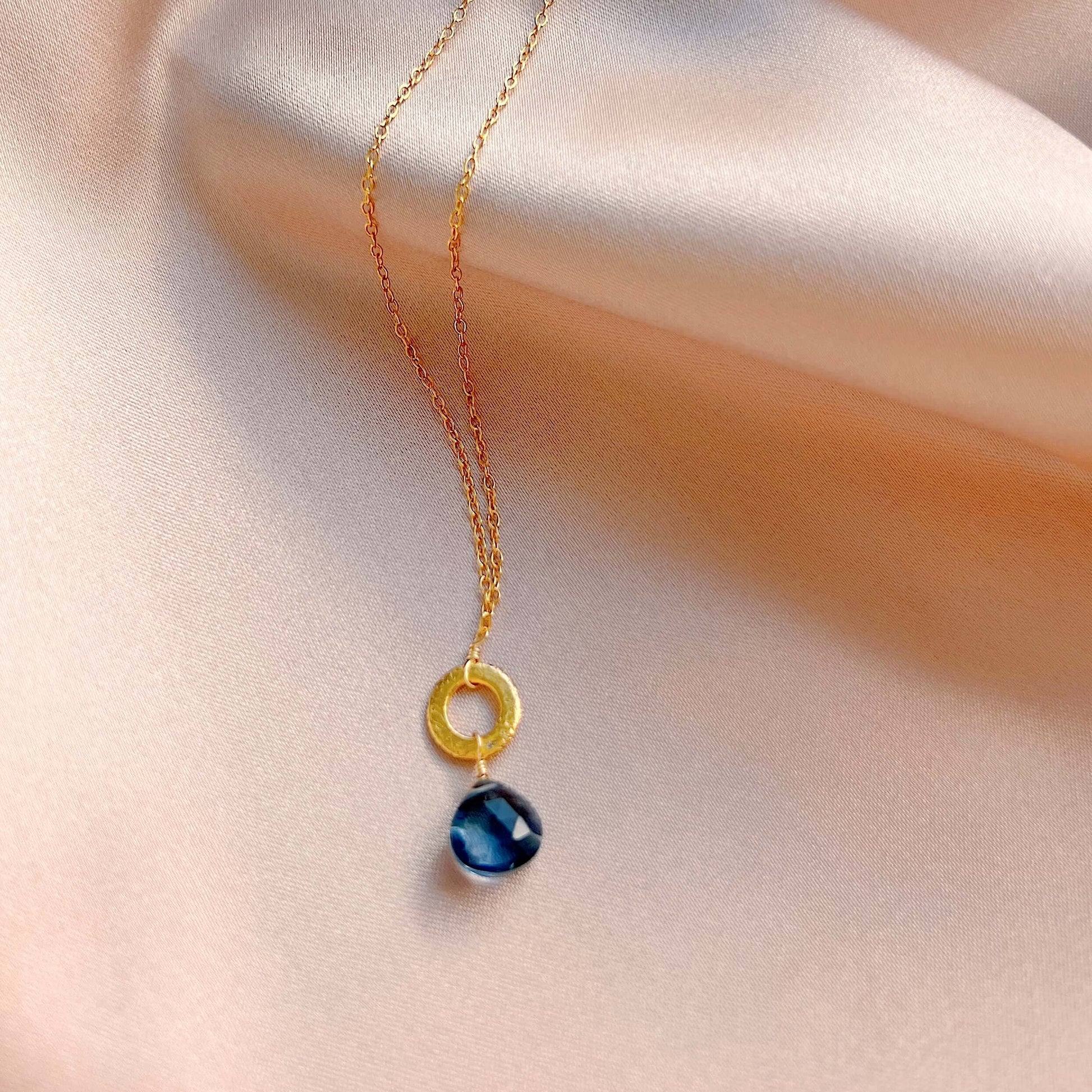 Necklace with a gold ring and blue pendant on a soft fabric background