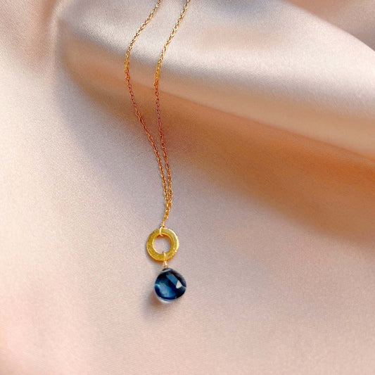Necklace with a gold ring and blue pendant on a soft fabric background