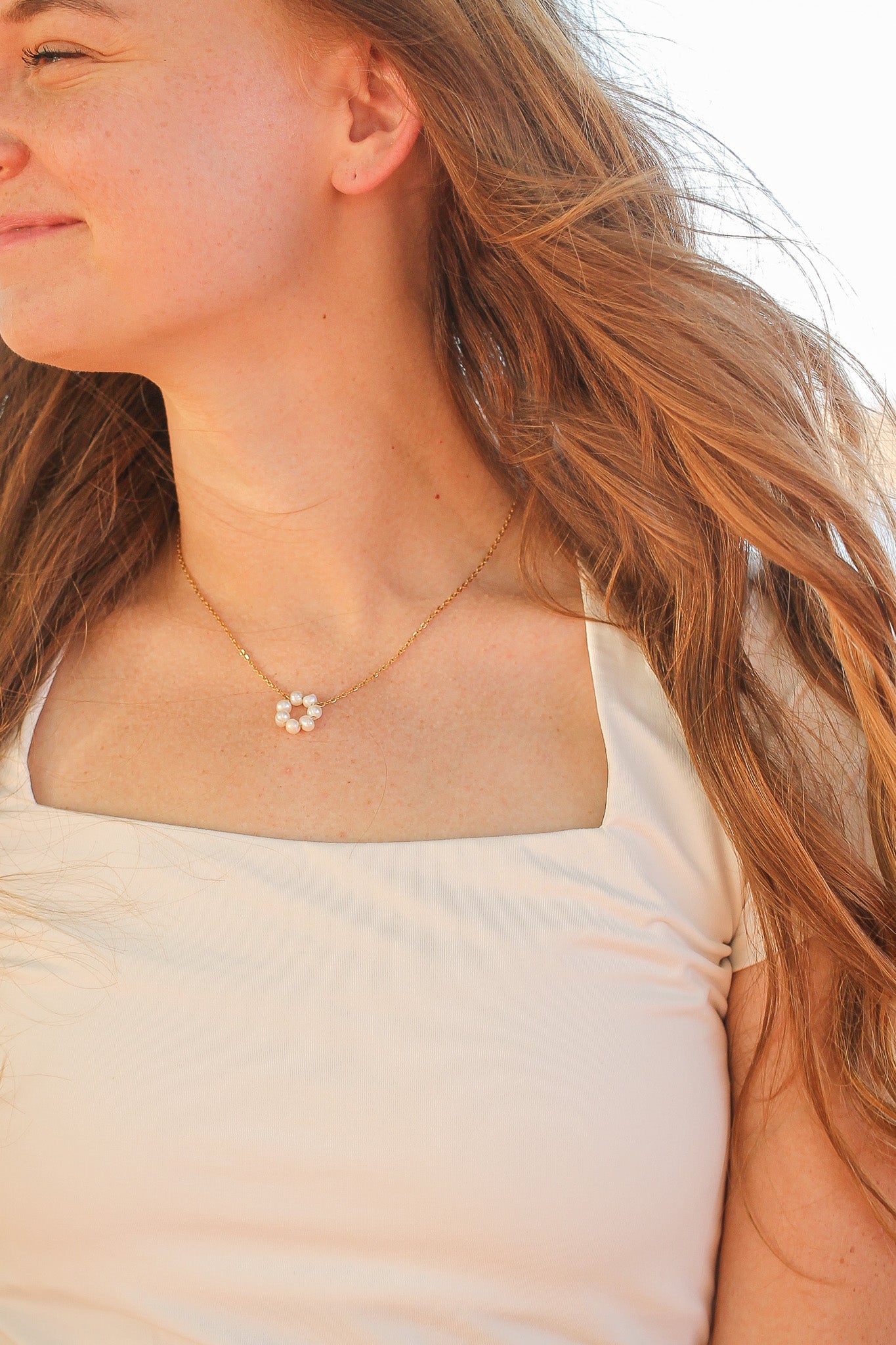 Close-up of a person wearing a delicate necklace with a small flower pendant.