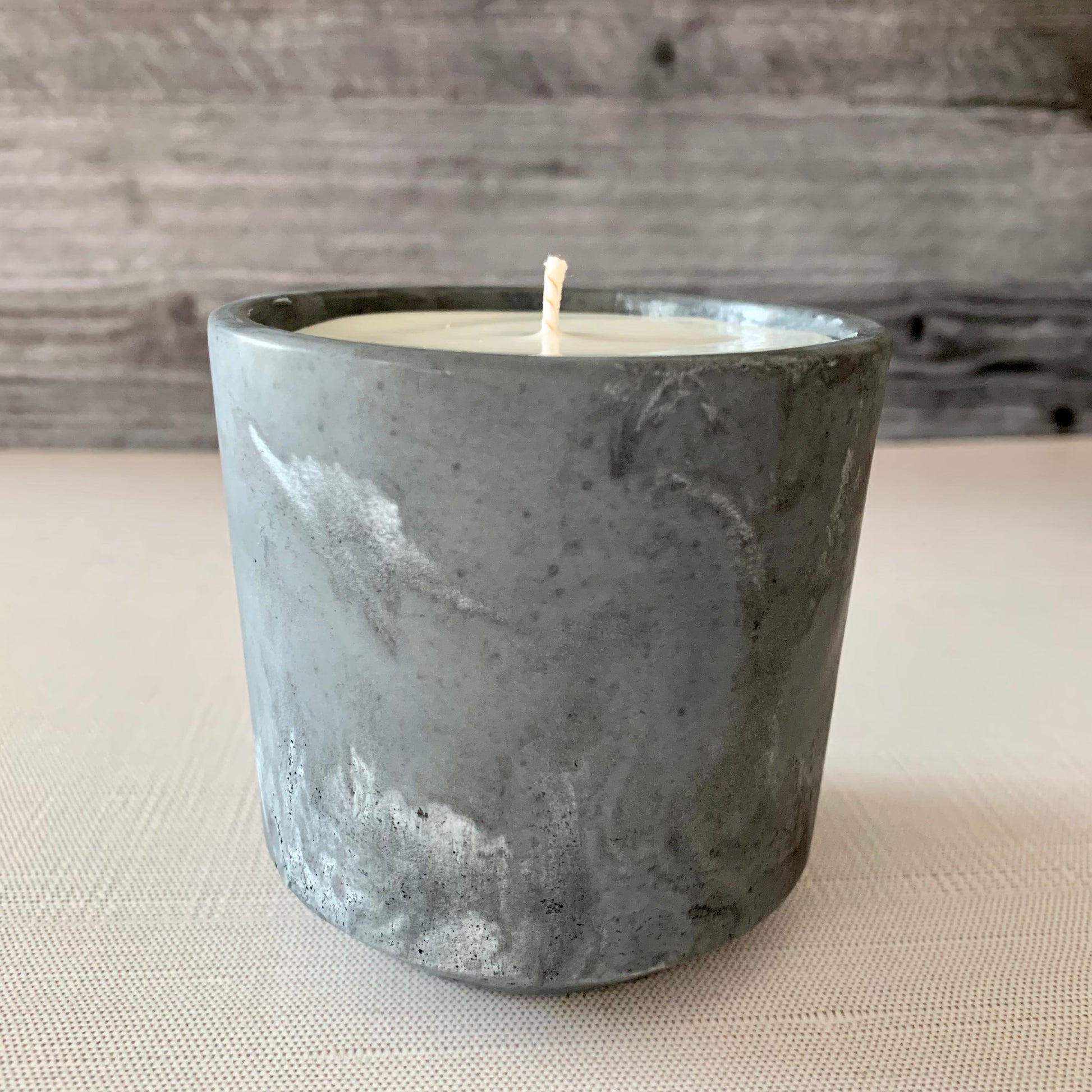 Candle in a gray concrete holder on a textured surface with a wooden background