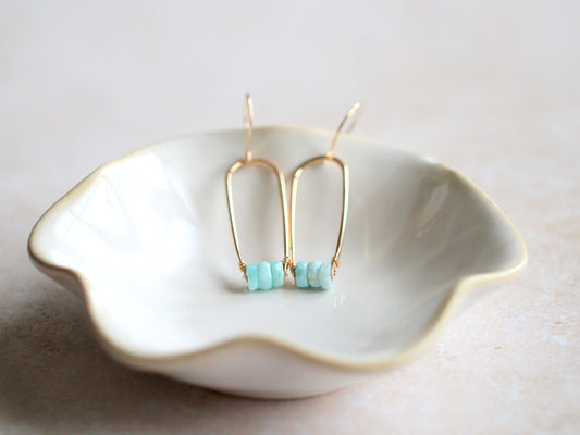 Gold earrings with turquoise beads on a white dish.