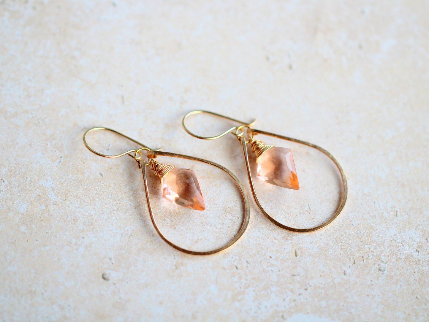 Gold hoop earrings with teardrop-shaped pink gemstones on a light beige background