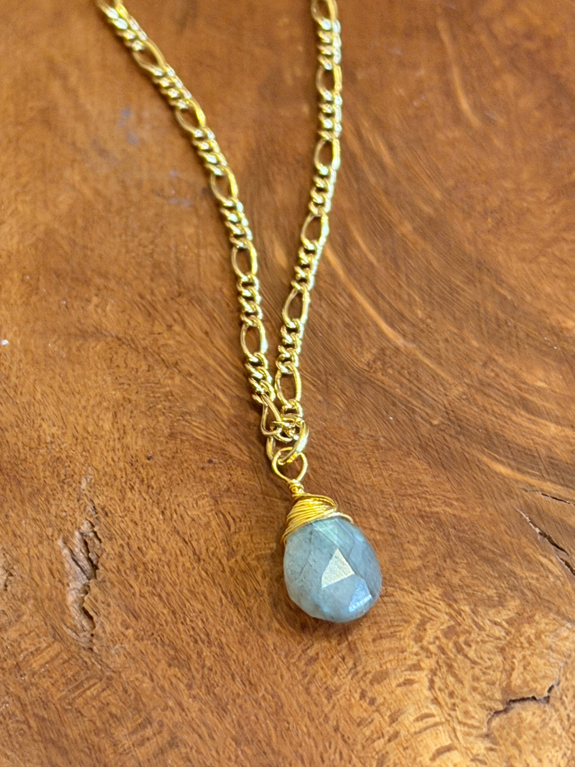 Necklace with a gold chain and blue laboradite gemstone on a wooden surface