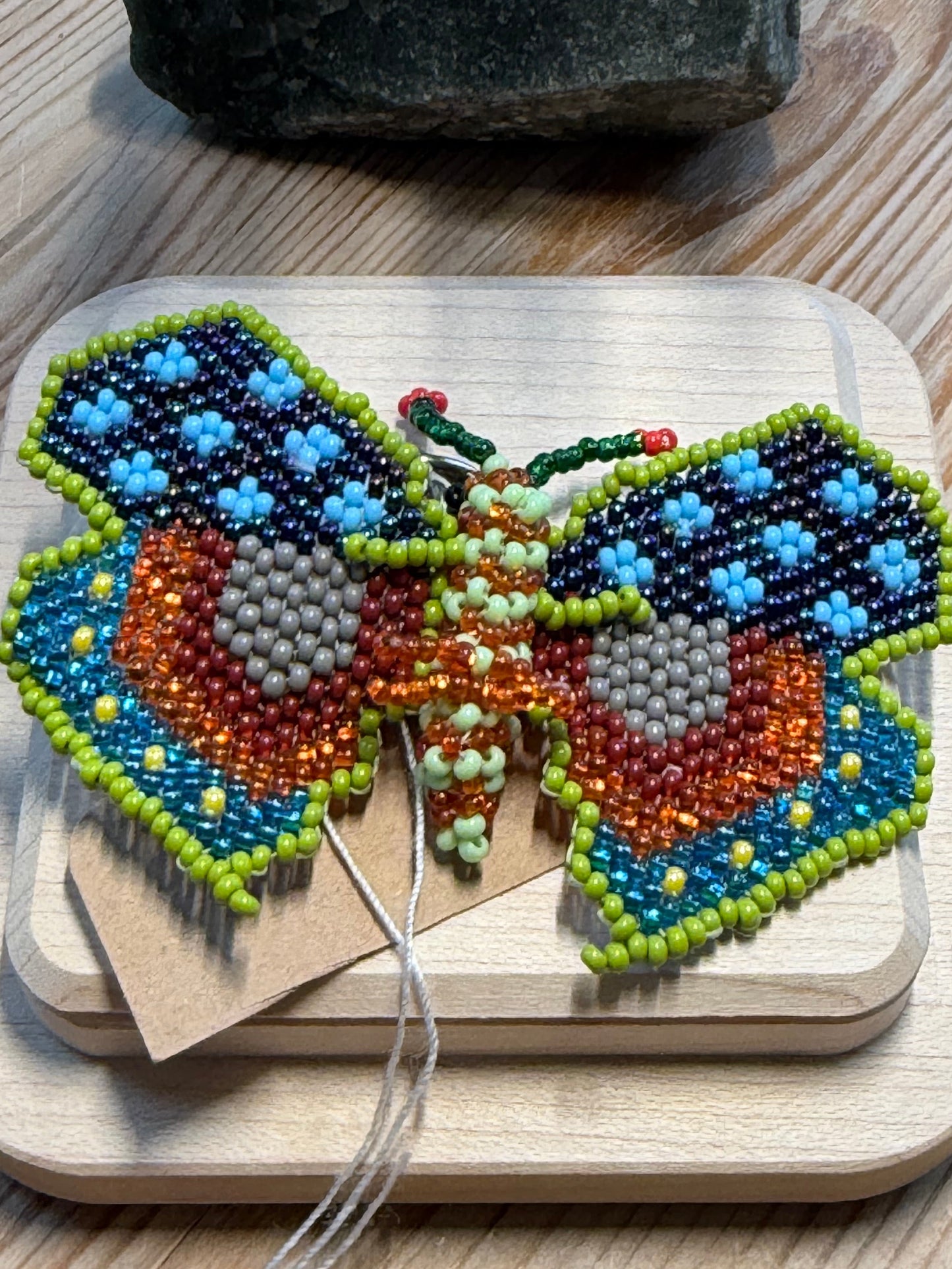 Colorful beaded butterfly ornament on a wooden board with a textured surface.
