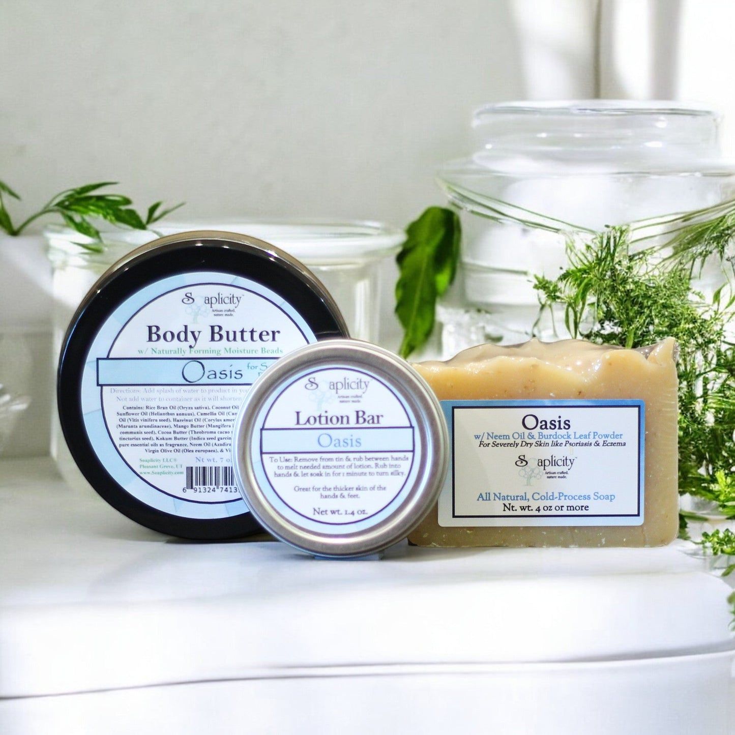 Body butter, lotion bar, and soap on a white surface with greenery in the background