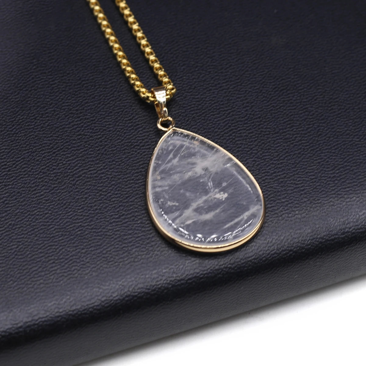 Teardrop-shaped pendant necklace on a gold chain against a dark blue background
