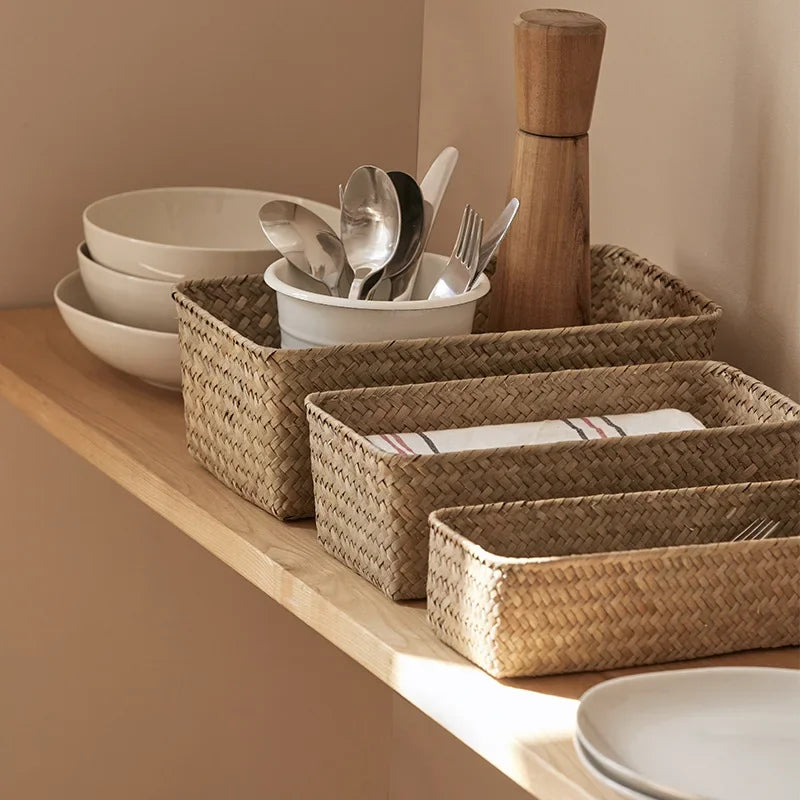 Woven baskets with cutlery and plates on a wooden shelf against a beige wall.