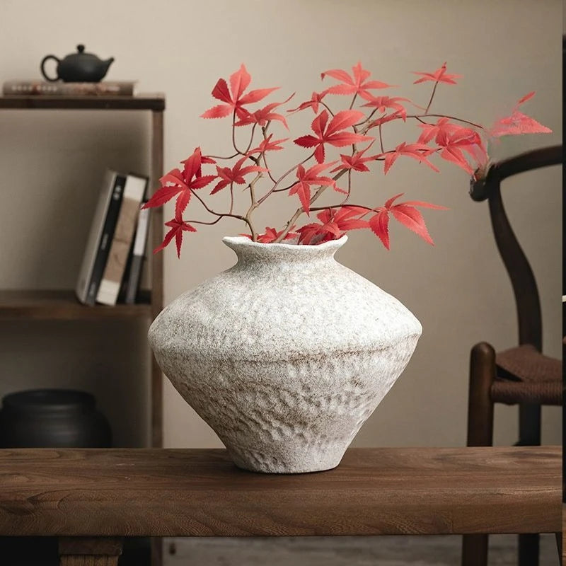 Textured white vase with red leaves on a wooden surface, blurred background