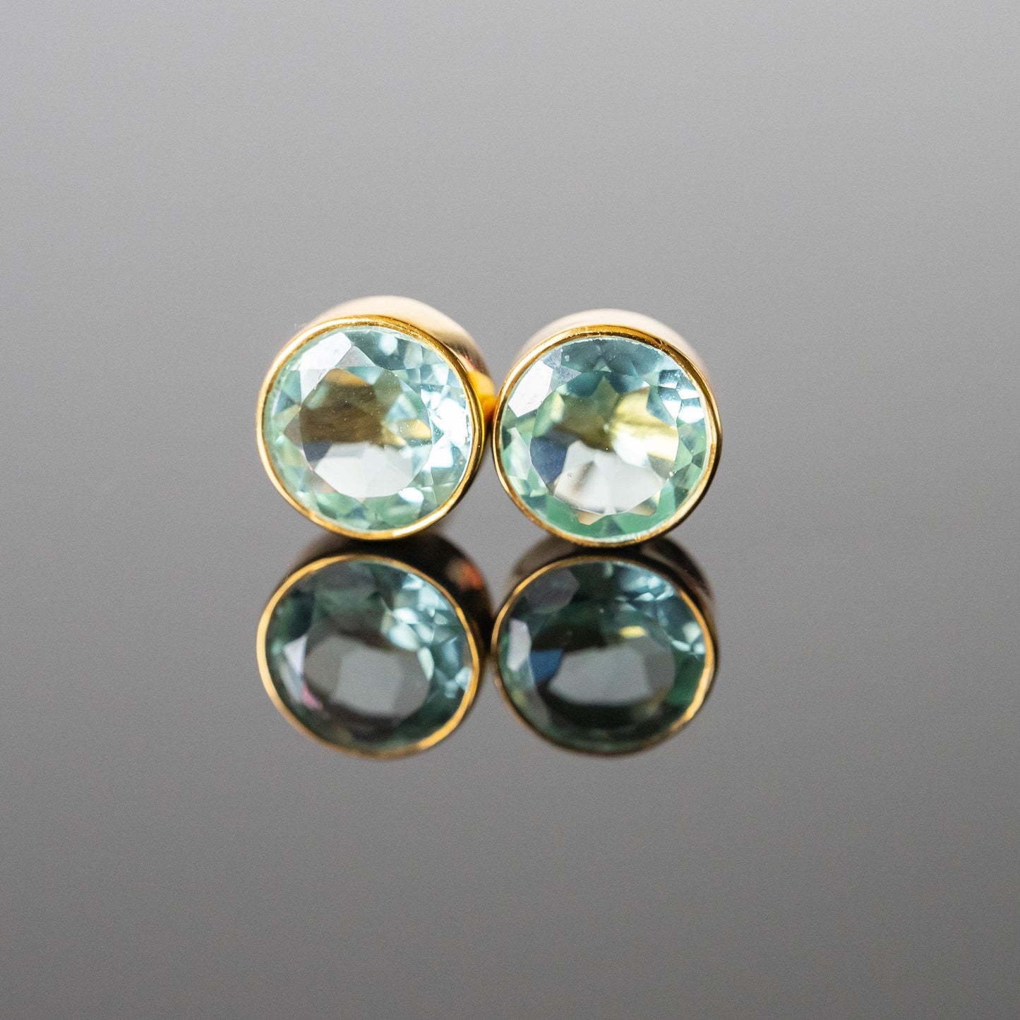 Pair of gold earrings with green gemstones on a reflective gray surface