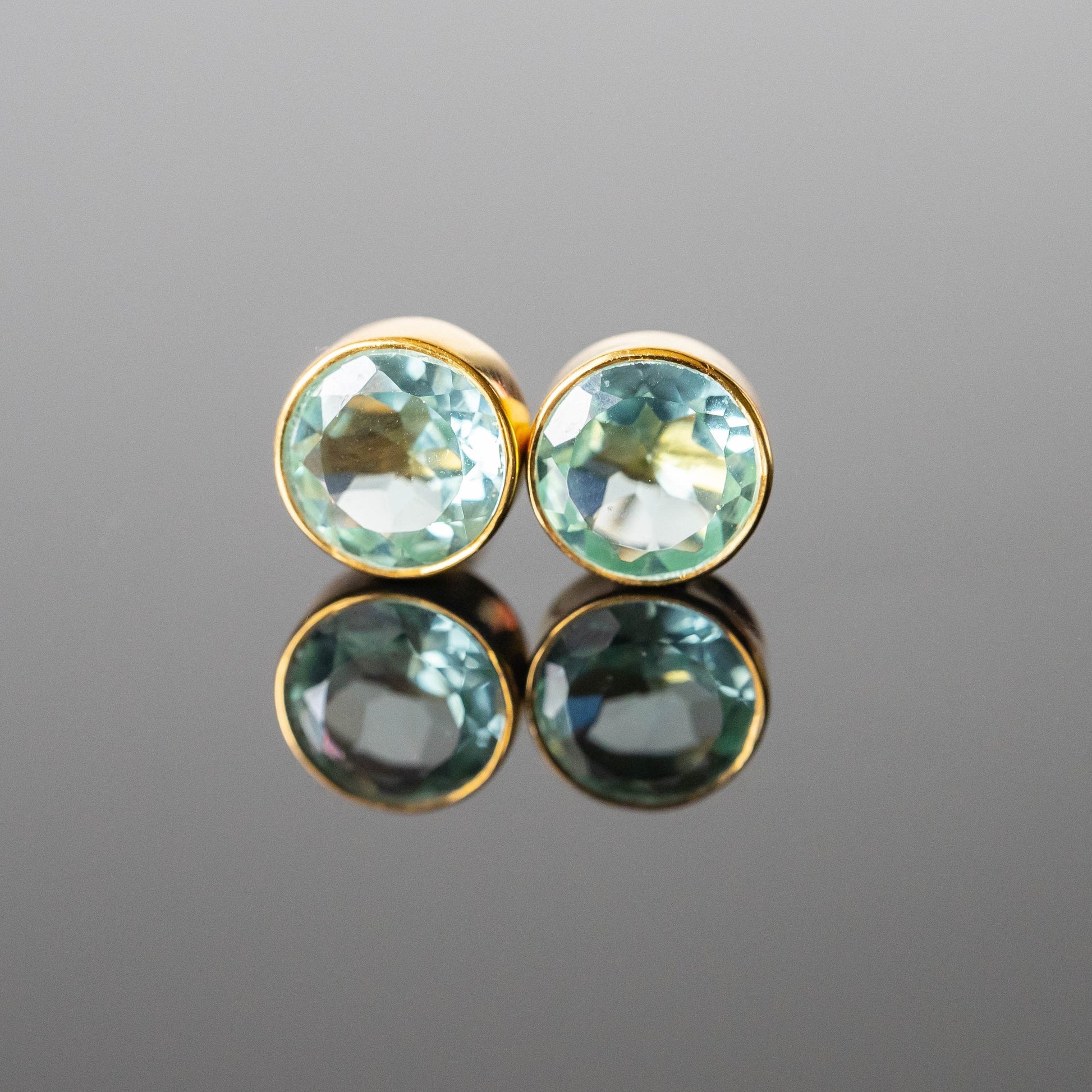 Pair of gold earrings with green gemstones on a reflective gray surface