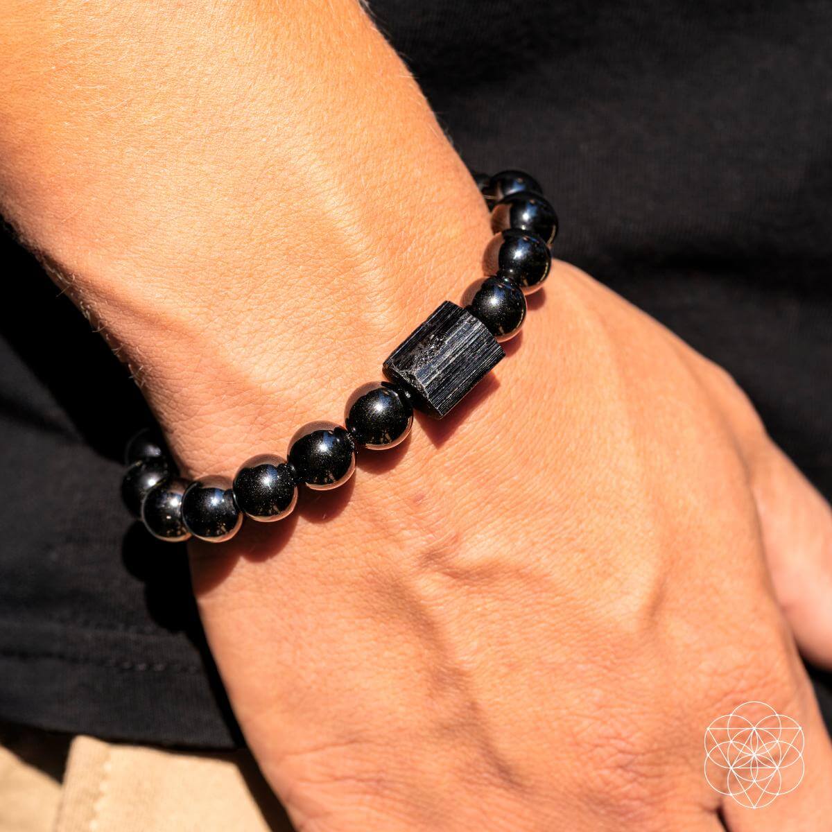 Black beaded bracelet with a large stone on a wrist against a neutral background