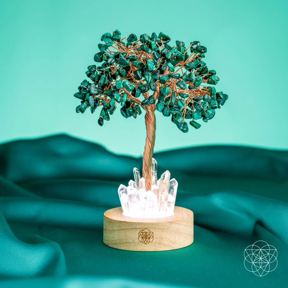 Decorative tree with green gemstones and crystal base on a teal fabric background