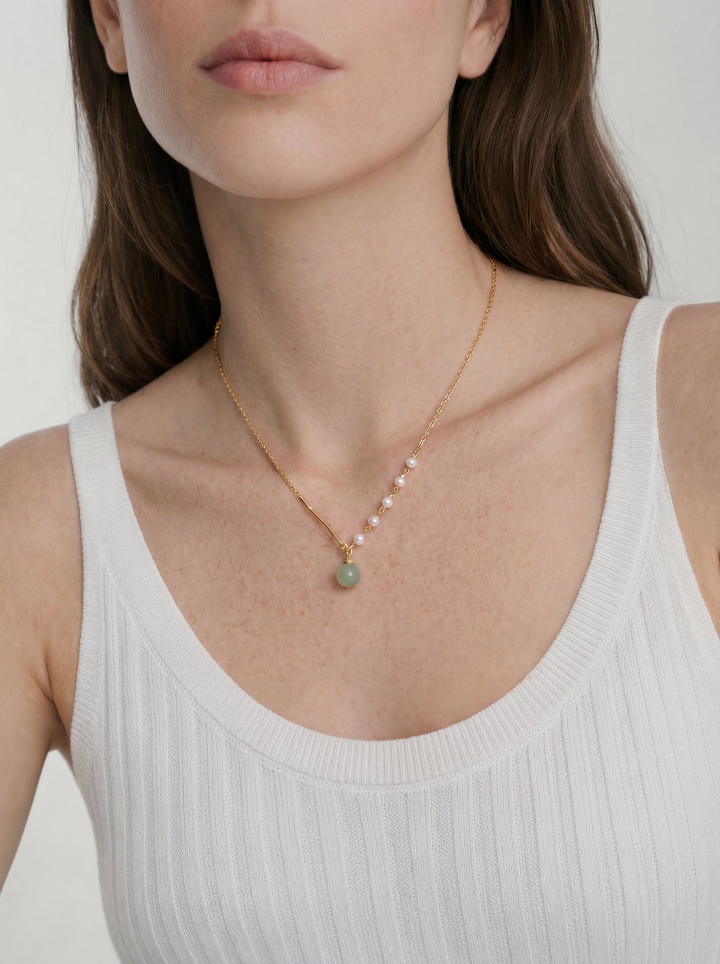Necklace with green pendant worn by a person in a white tank top on a plain background